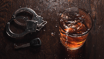 a glass of liquor with handcuffs and a key on the side, representing DUI